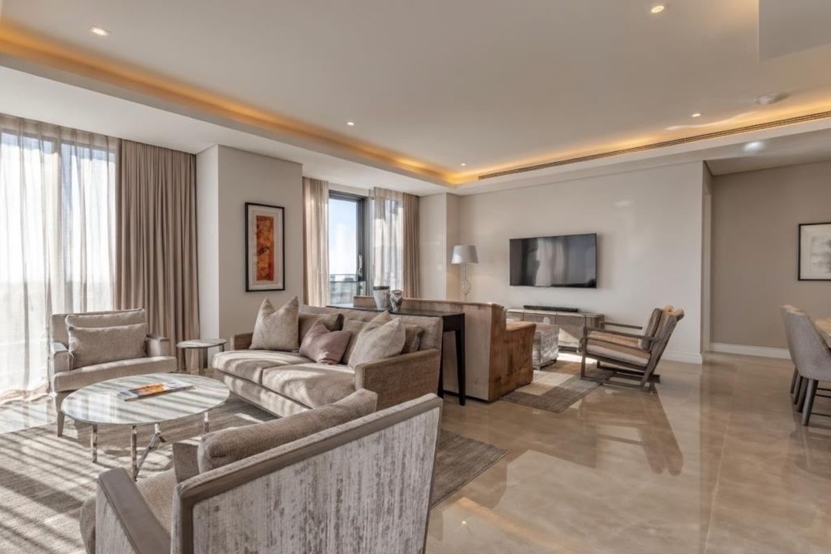 A spacious, modern living room featuring high-quality large format floor tiles, recessed cove lighting, and floor-to-ceiling window treatments.
