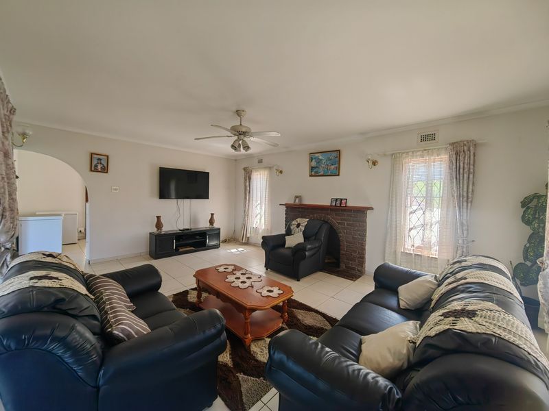 Spacious living room featuring a classic brick fireplace, ceiling fan, and neutral tiled flooring, offering a comfortable and functional family space.
