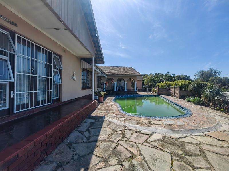 Rear exterior view featuring a swimming pool with stone paving, a brick retaining wall, and a covered patio area.