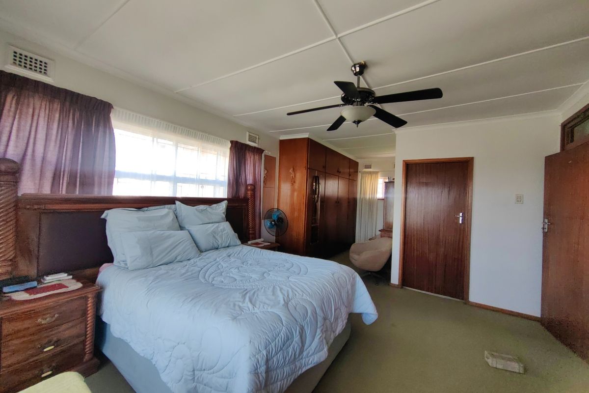 Spacious bedroom featuring built-in timber cupboards, a ceiling fan, and large windows allowing for natural light.