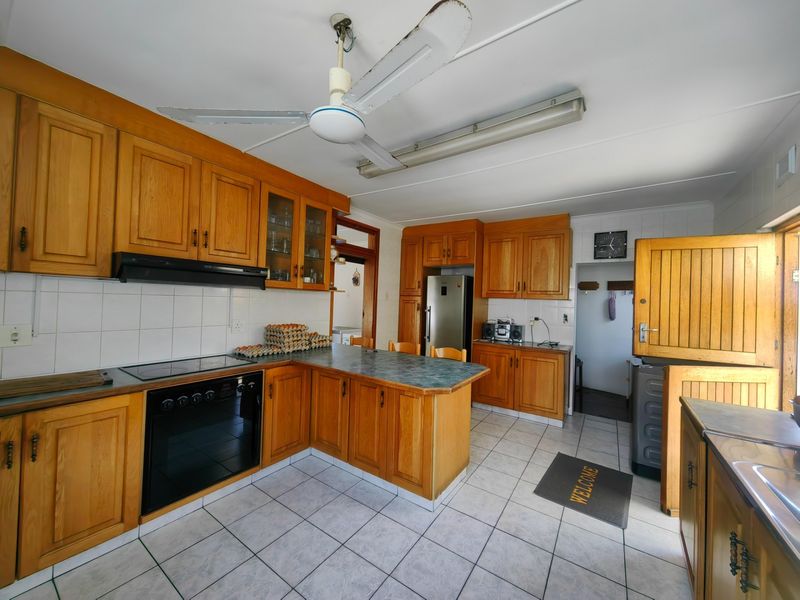 A functional kitchen featuring wooden cabinetry, tiled flooring, built-in oven and hob, and a classic stable door leading to the exterior.