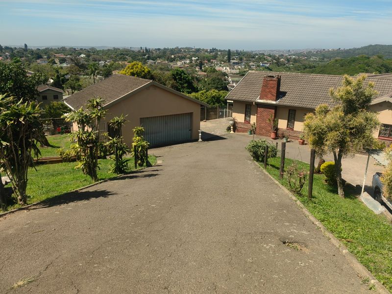 Elevated view of the property featuring a long asphalt driveway, detached garage, and main house with a brick chimney and tiled roof.