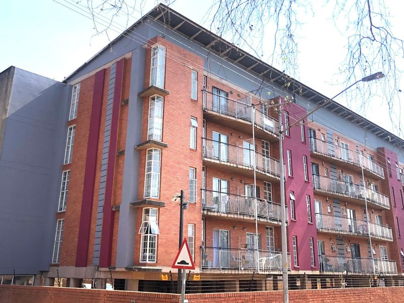 A multi-story apartment building featuring a brick and painted facade with multiple balconies and secure perimeter fencing.