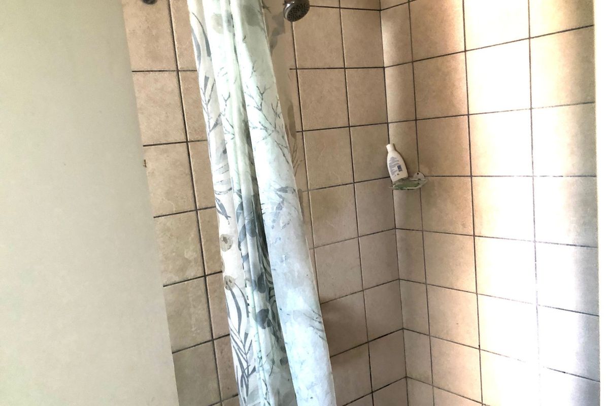A shower enclosure featuring dated ceramic wall tiles and a standard shower head, showing signs of wear in the grout lines.