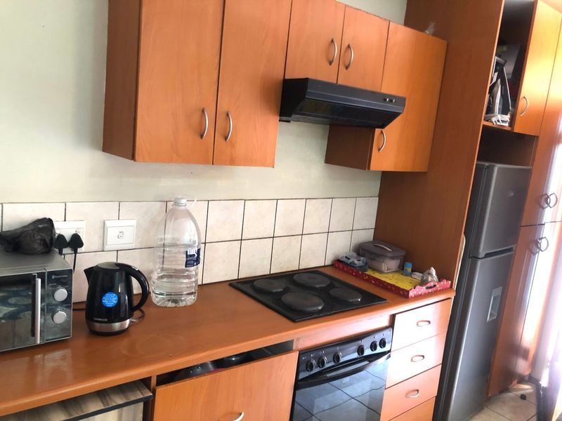 A functional kitchen featuring wood-look laminate cabinetry, a tiled backsplash, built-in oven, electric hob, and an integrated extractor fan.