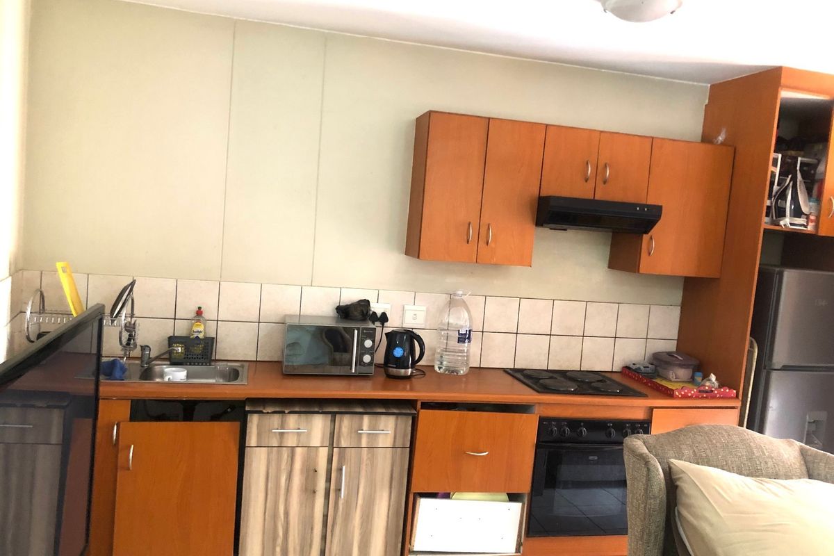 A dated kitchen featuring wood-look cabinetry, a built-in oven with electric hob, and a tiled backsplash, currently showing signs of wear and maintenance needs.