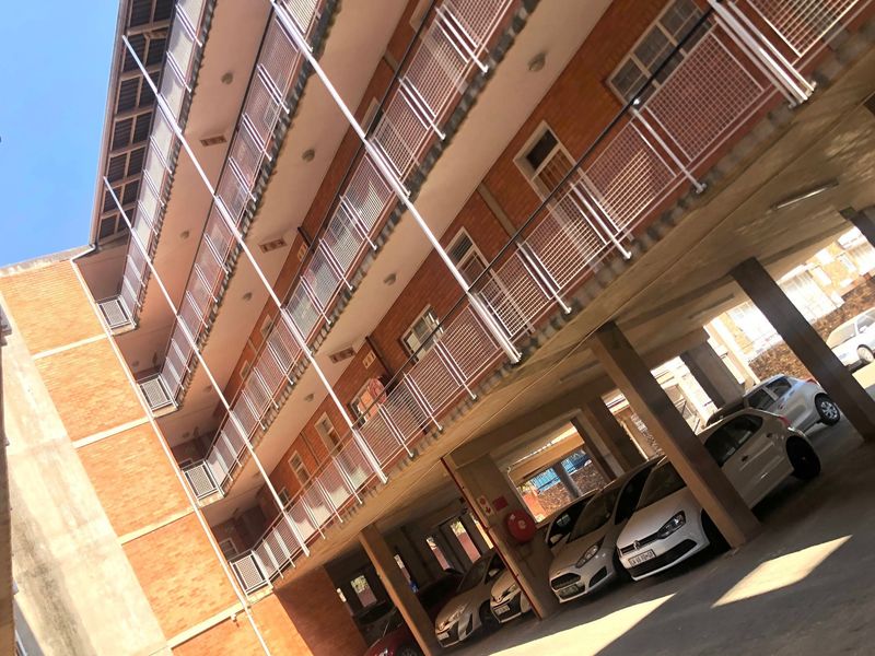 Exterior view of a multi-story brick apartment building featuring covered ground-level parking and metal balcony railings.