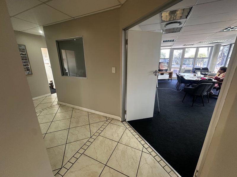 Office suite featuring a tiled hallway leading into a carpeted workspace with large windows, recessed lighting, and an internal glass partition.