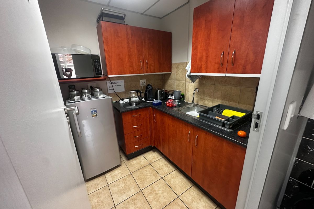 A compact office kitchenette featuring wood-finish cabinetry, dark laminate countertops, a stainless steel sink, and tiled flooring.