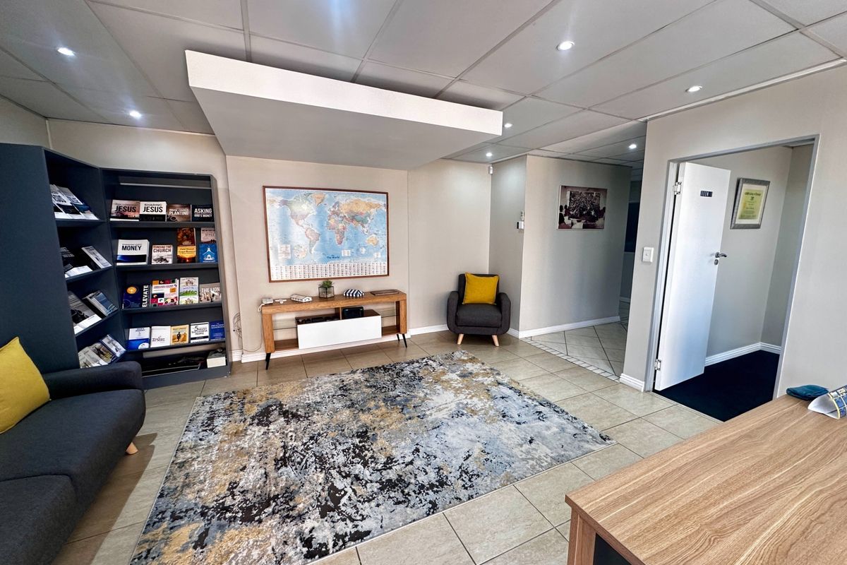 A well-maintained office reception area featuring tiled flooring, a suspended ceiling with recessed lighting, and a built-in shelving unit.