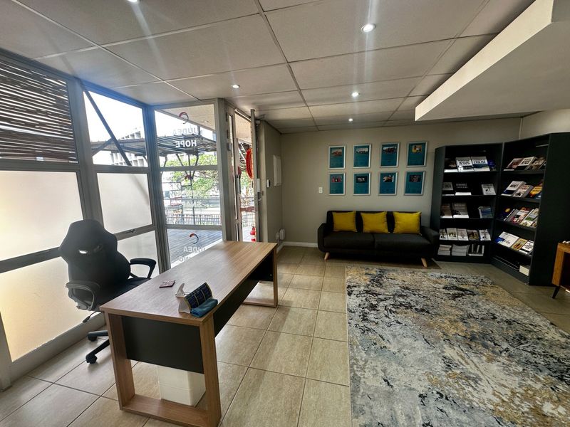 A professional office space featuring tiled flooring, a suspended ceiling with recessed lighting, and large glass windows providing natural light and exterior access.