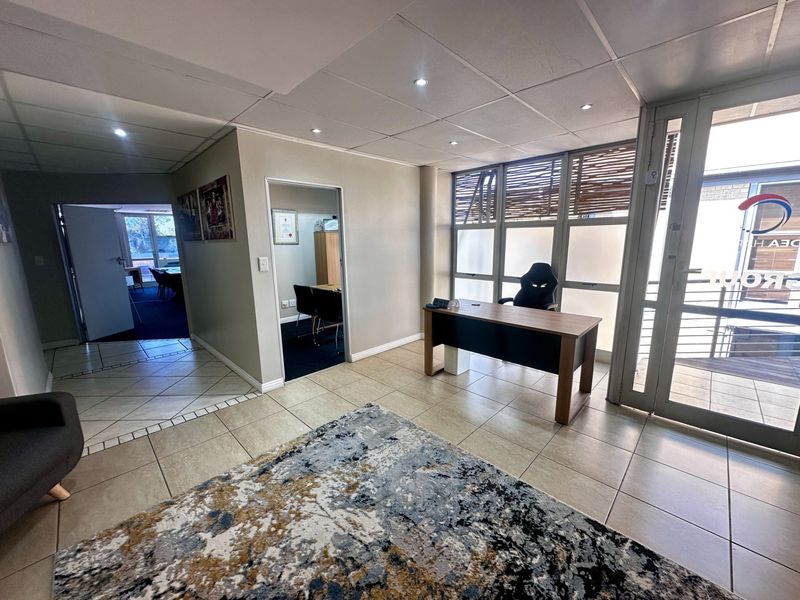 A bright office space featuring tiled flooring, a suspended ceiling with recessed lighting, and large windows providing natural light.