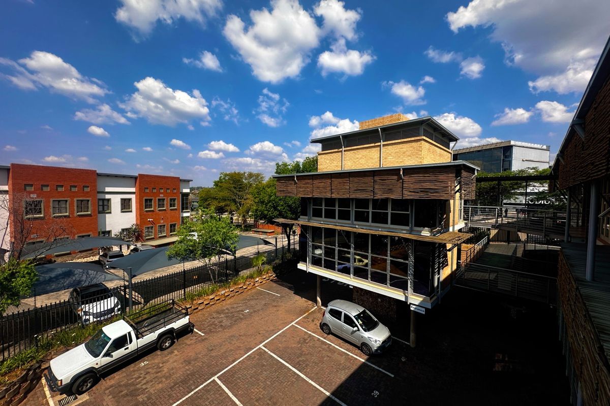 An elevated view of a modern office complex featuring a multi-level building, paved parking area with shade ports, and secure perimeter fencing.
