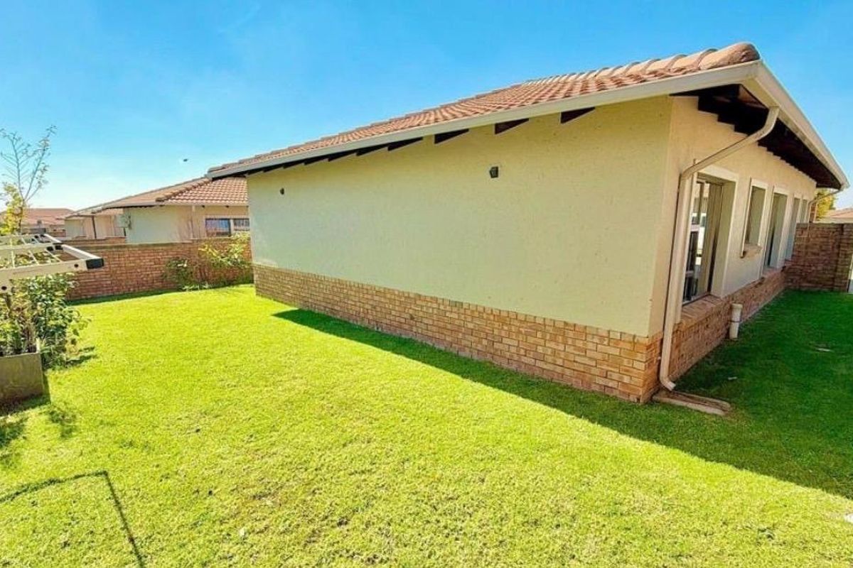 A view of the rear garden featuring a well-maintained lawn, brick perimeter wall, and the rear facade of the house with a tiled roof.