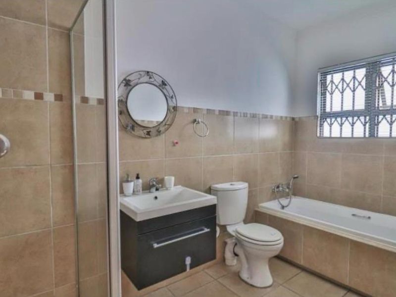 A functional bathroom featuring a vanity cabinet, bathtub, separate shower enclosure, and neutral wall tiling with security bars on the window.