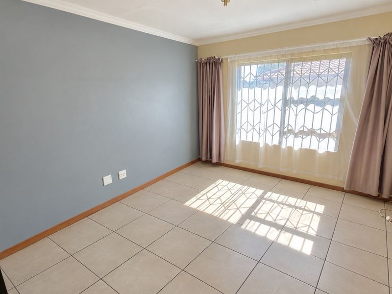 A bright, empty bedroom featuring neutral tiled flooring, a feature wall, and a window fitted with security bars.