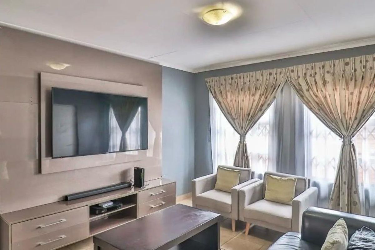 A comfortable living room featuring a modern built-in media unit, tiled flooring, and large windows allowing for natural light.