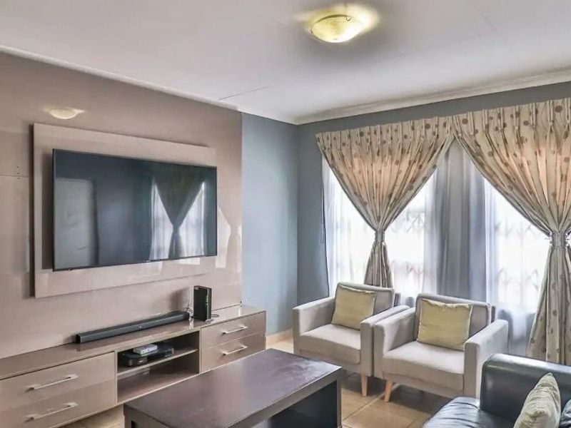 A comfortable living room featuring a modern built-in media unit, tiled flooring, and large windows allowing for natural light.