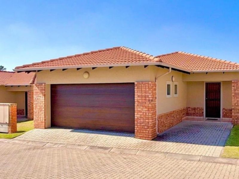 Front view of a well-maintained single-story house featuring a tiled roof, brick accents, a double garage, and a paved driveway.