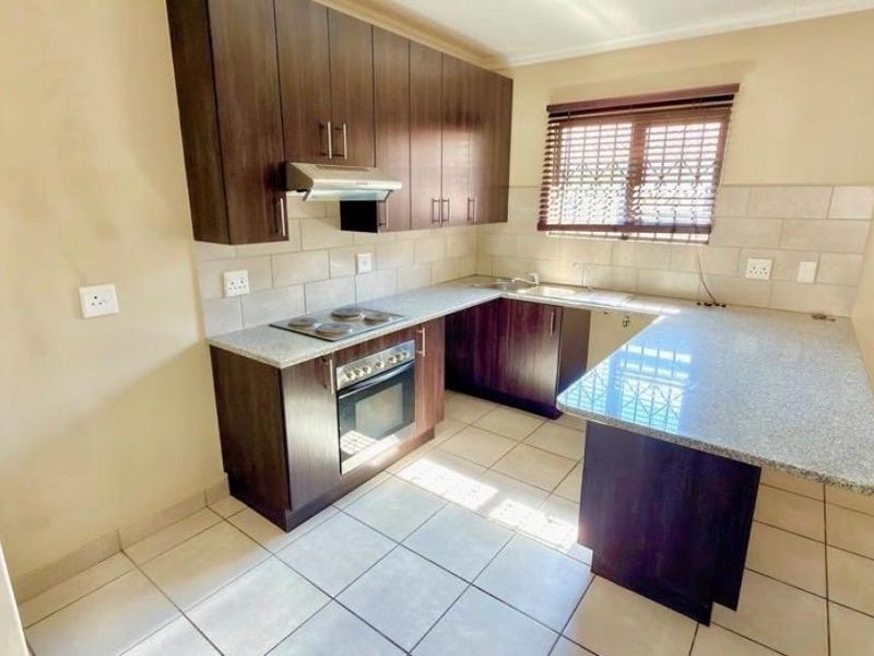 A functional kitchen featuring dark wood cabinetry, granite countertops, a built-in oven, electric hob, and tiled flooring with a breakfast nook extension.