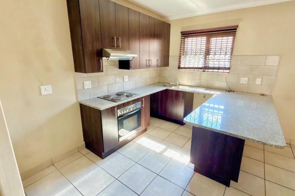 A functional kitchen featuring dark wood cabinetry, granite countertops, a built-in oven, electric hob, and tiled flooring with a breakfast nook extension.