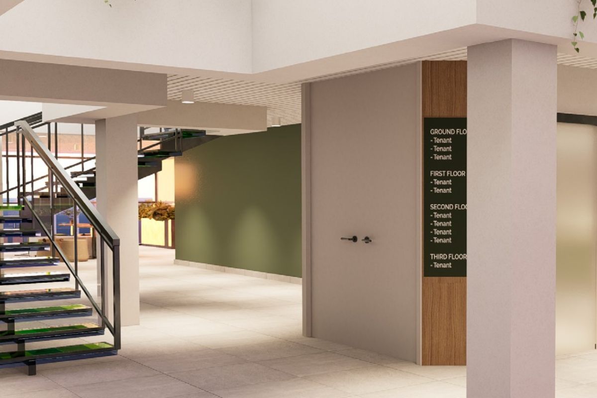 Modern commercial building lobby featuring a central staircase, tiled flooring, and a clear tenant directory signage board.