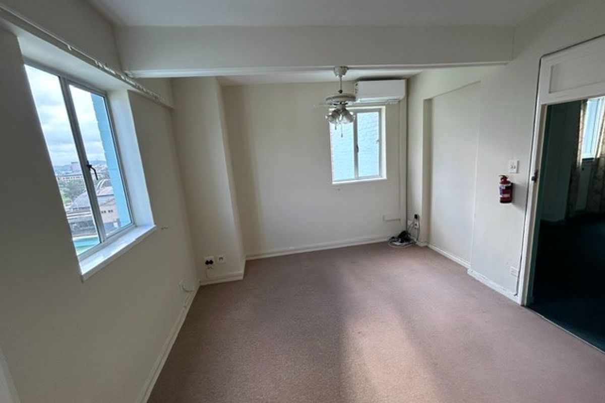 A vacant bedroom featuring neutral walls, carpeted flooring, a ceiling fan, and a wall-mounted air conditioning unit.