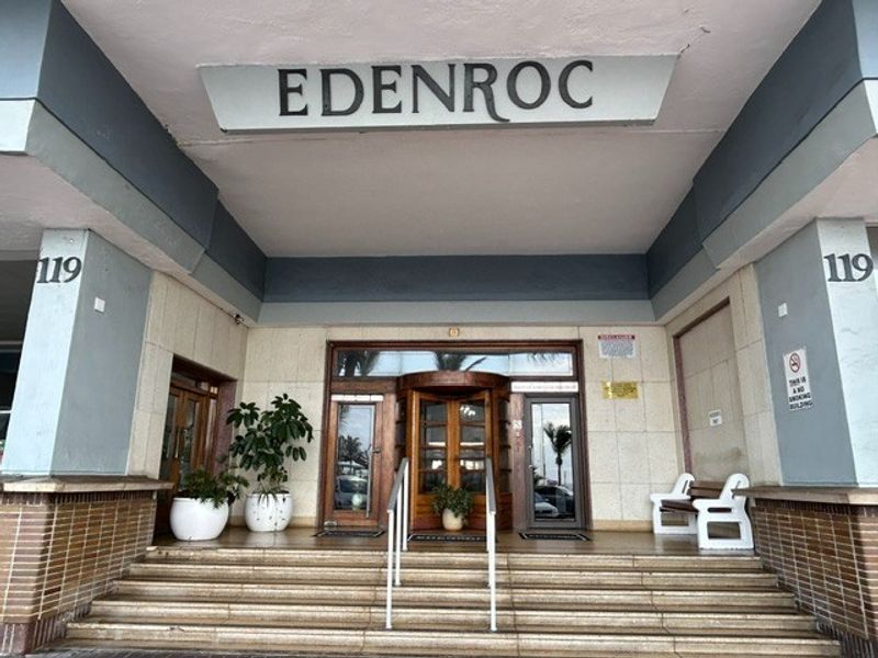 The main entrance of Edenroc retirement village featuring a revolving door, stone facade, and concrete staircase with metal handrails.
