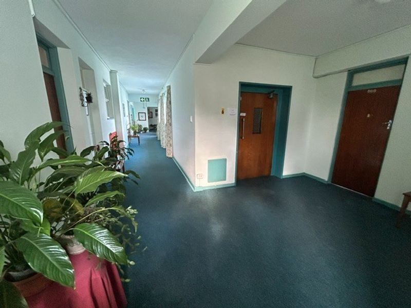 A wide retirement village hallway featuring carpeted flooring and multiple unit access doors, providing a functional and accessible corridor space.