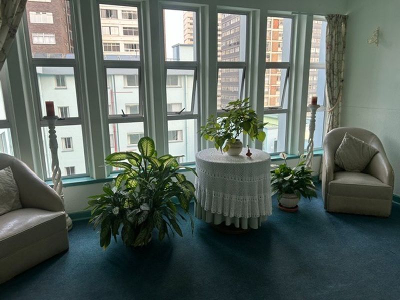 A bright living area featuring a wall of large windows providing ample natural light and an urban outlook.