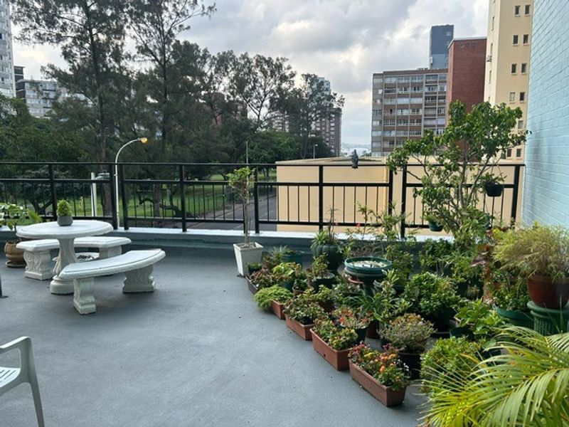 A spacious outdoor balcony featuring a metal balustrade and concrete flooring, offering an elevated view of the surrounding urban landscape.