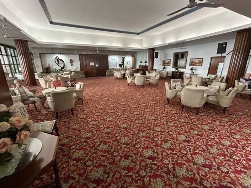 Spacious communal lounge area within the retirement village, featuring high ceilings, decorative columns, and traditional patterned carpeting.