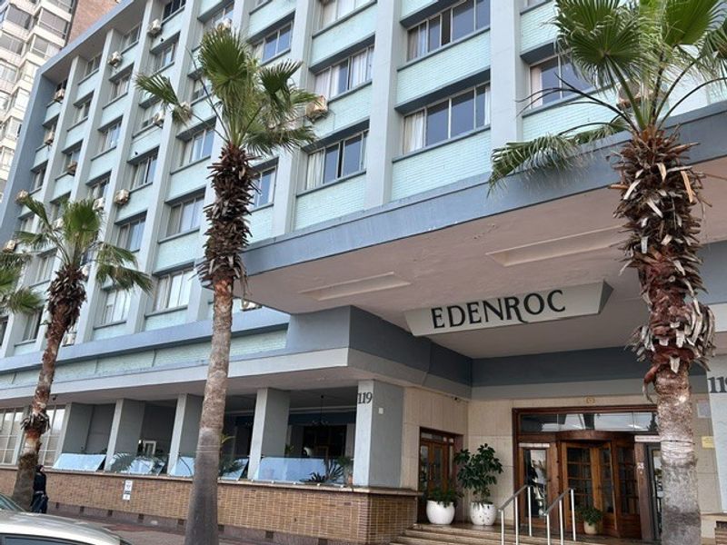 Front elevation of the Edenroc retirement village building, featuring a multi-story facade, concrete entrance canopy, and established palm tree landscaping.