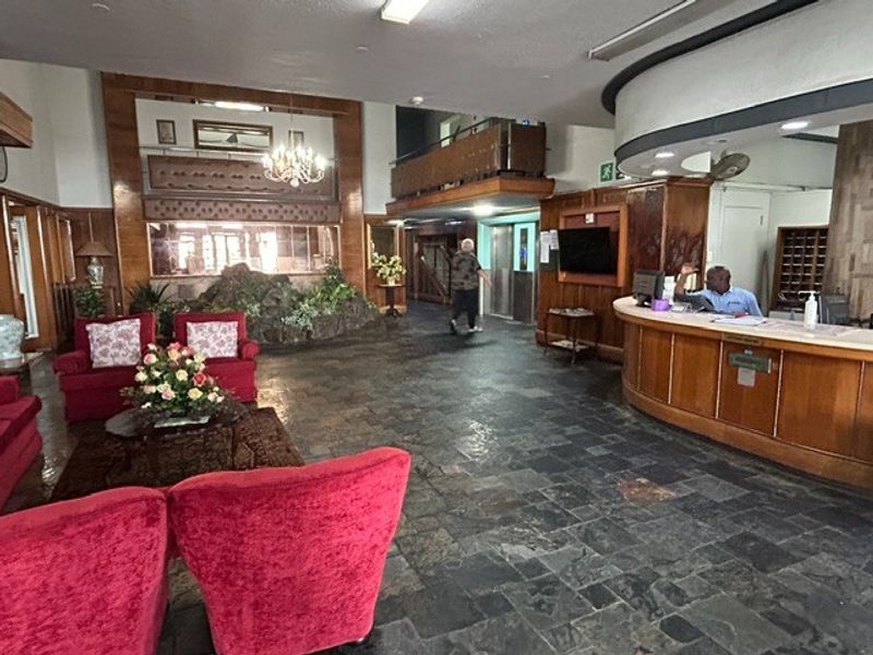 Spacious retirement village clubhouse lobby featuring a reception desk, stone flooring, and built-in wood paneling with an integrated elevator and indoor rock feature.