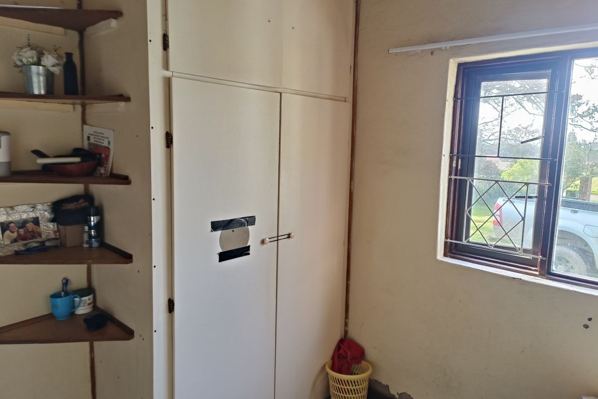 A bedroom featuring a built-in wardrobe with corner shelving and a window fitted with security bars, requiring cosmetic updates to wall finishes.