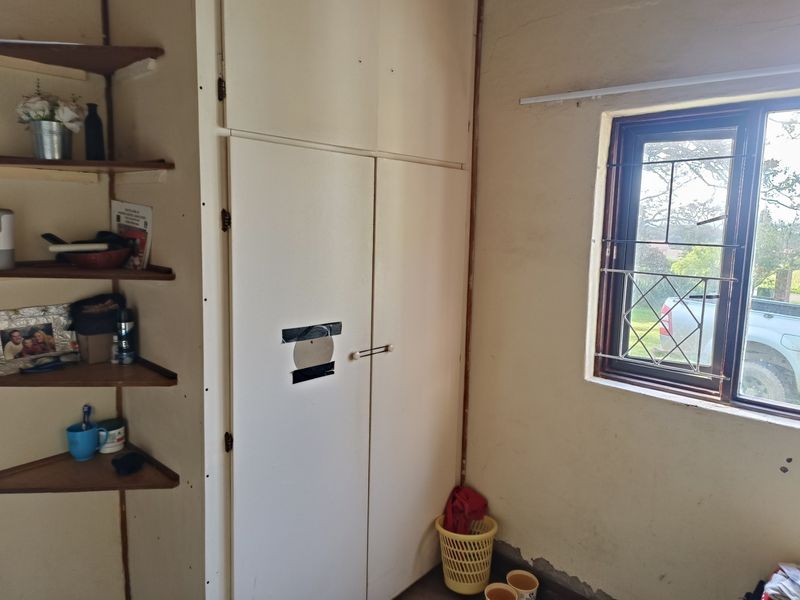 A bedroom featuring a built-in wardrobe with corner shelving and a window fitted with security bars, requiring cosmetic updates to wall finishes.