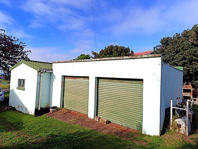 A detached double garage featuring roller doors and a combination of pitched and flat roof sections, set within a grassed yard area.