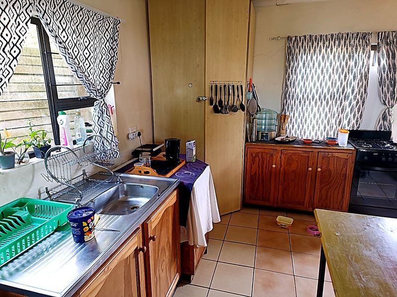 A functional kitchen featuring wooden cabinetry, a stainless steel sink, tiled flooring, and a built-in oven, offering potential for cosmetic updates.
