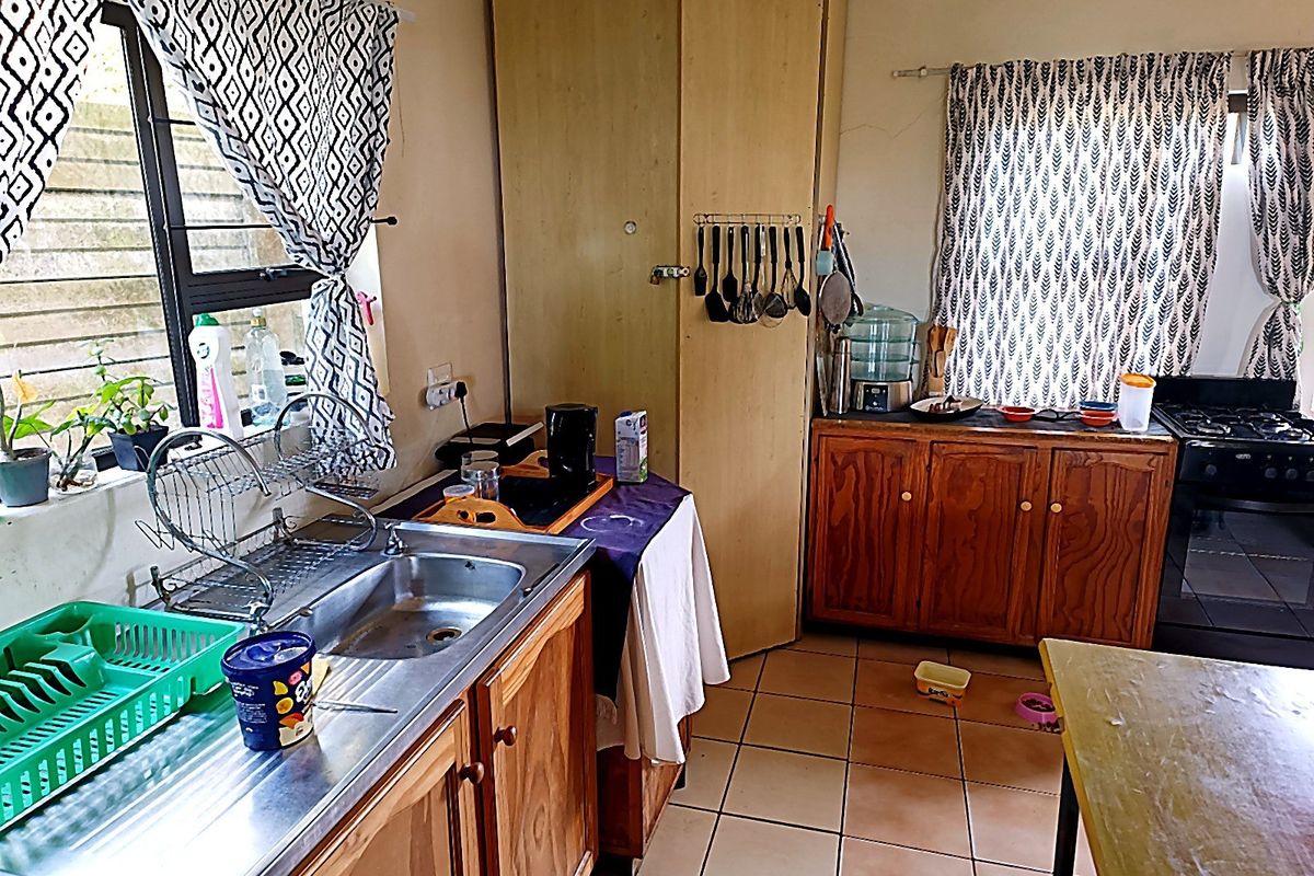 A functional kitchen featuring wooden cabinetry, a stainless steel sink, tiled flooring, and a built-in oven, offering potential for cosmetic updates.