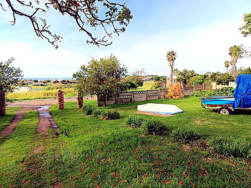 A spacious grassy garden area featuring a precast concrete boundary wall and brick pillars, offering an open outdoor space with distant coastal views.