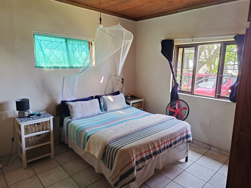 A functional bedroom featuring tiled flooring, timber ceiling panels, and windows fitted with security burglar bars.
