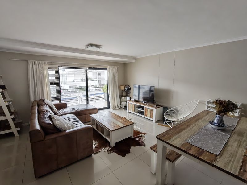 An open-plan living and dining area featuring neutral walls, tiled flooring, and a large sliding glass door providing access to the balcony.
