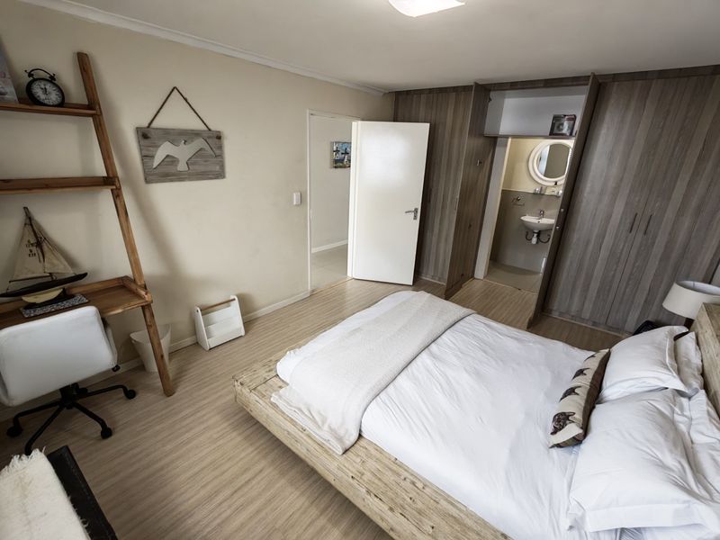 A well-maintained bedroom featuring light laminate flooring, extensive built-in cabinetry, and direct access to an en-suite bathroom.