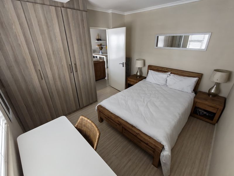 A well-maintained bedroom featuring light-toned laminate flooring and ample built-in cupboard storage, with a neutral color palette and direct access to an adjacent living area.
