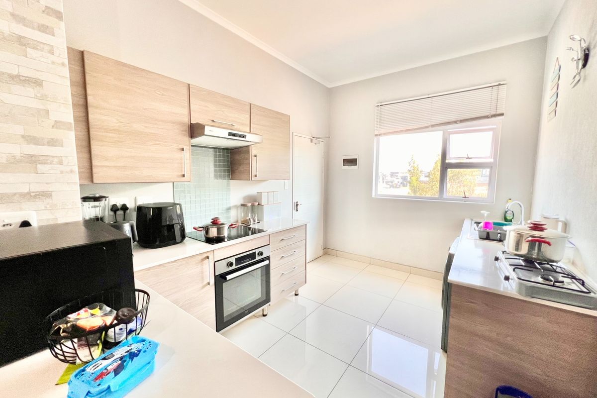 Modern kitchen featuring light wood-finish cabinetry, stone countertops, integrated oven and hob, tiled flooring, and a functional layout with ample workspace.