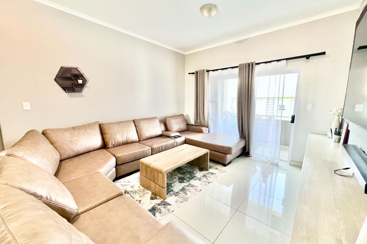 A bright living room featuring polished porcelain floor tiles and a sliding glass door providing access to an outdoor balcony area.