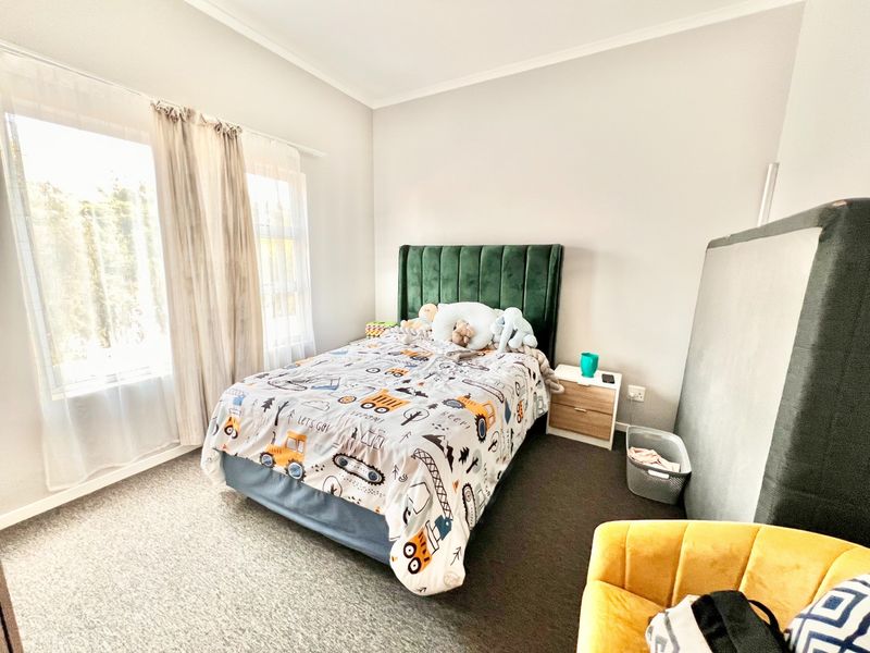 A well-lit bedroom featuring neutral wall finishes, carpeted flooring, and a large window allowing for ample natural light.
