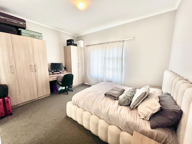A functional bedroom featuring built-in cupboards, carpeted flooring, and a window with curtain rails, providing a practical living space.