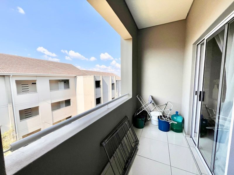 A covered balcony featuring tiled flooring and a metal balustrade, offering an open view of the surrounding apartment complex.