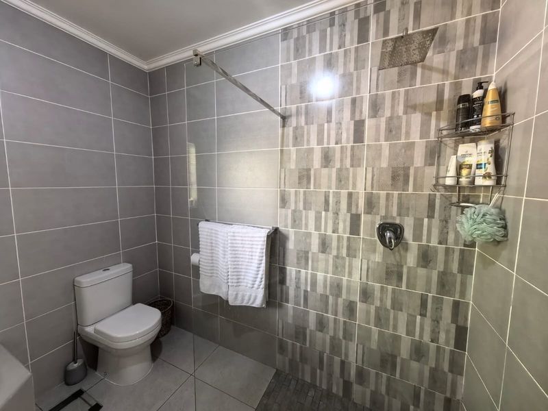 Modern bathroom featuring a walk-in shower with a glass screen, rainfall shower head, and contemporary grey tiled finishes throughout.